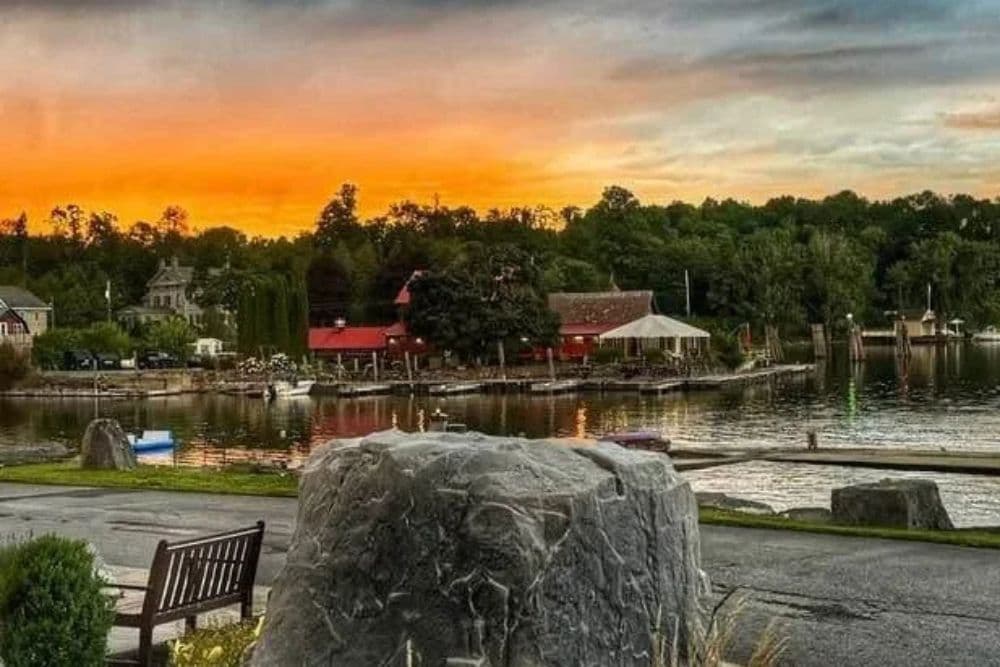 Sunset over a calm lake with charming buildings and boats reflected in the water.